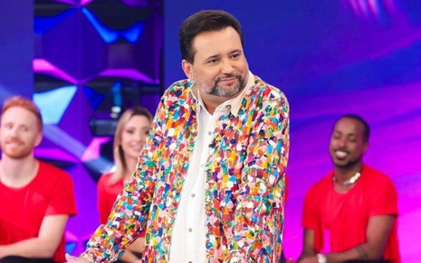 Geraldo Luís usando terno colorido no cenário do Programa Silvio Santos