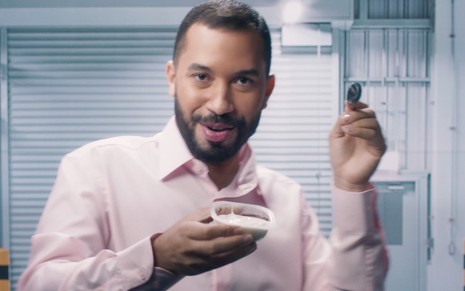 Gilberto Nogueira com uma camisa rosa, segurando um pote de iogurte e uma colher