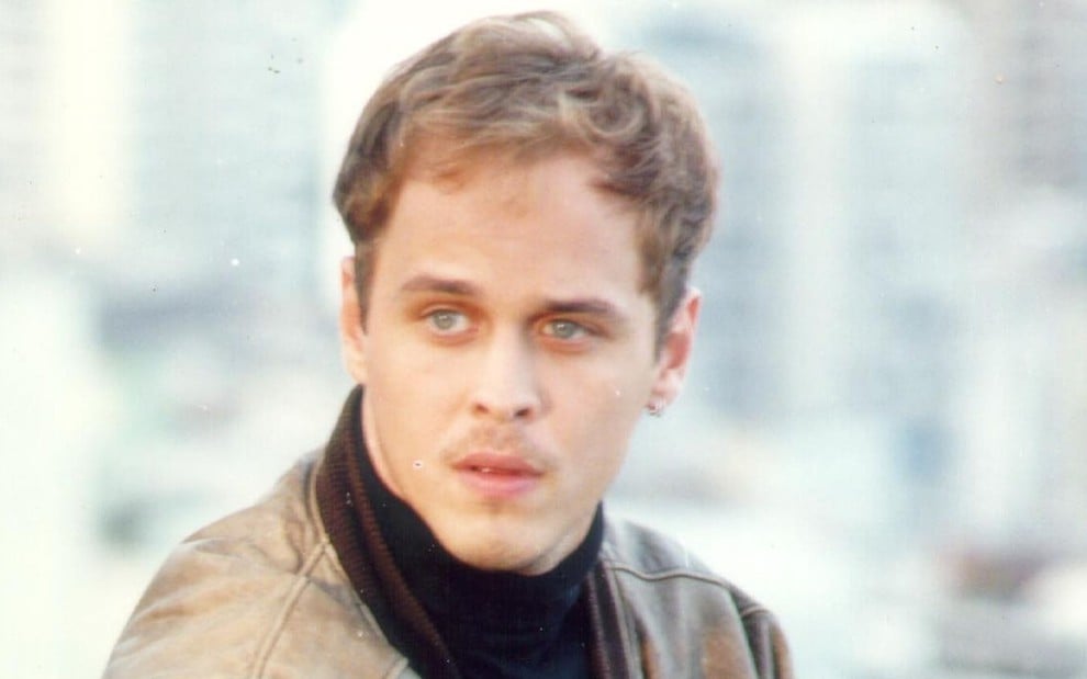 Guilherme Fontes como Alexandre de A Viagem (1994): ator olha para o horizonte, usa jaqueta marrom e blusa com gola rolê preta