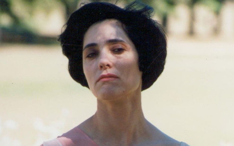 Christiane Torloni caracterizada como Diná em A Viagem (1994): atriz está com cabelo curto e usa regata branca e um bata transparente por si