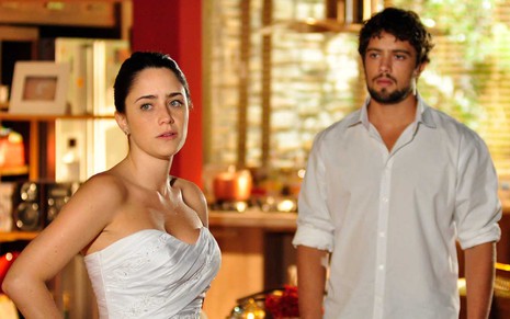 Com um vestido de noiva, a atriz Fernanda Vasconcellos coloca as mãos na cintura em indignação como Ana enquanto é observada por Rafael Cardoso, o Rodrigo, em cena de A Vida da Gente
