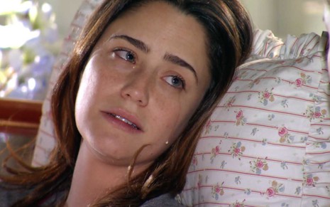 A atriz Fernanda Vasconcellos está prostrada em uma cama e chora, com lágrimas rolando pelas suas bochechas, como a Ana em A Vida da Gente