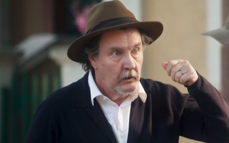 O ator Antonio Calloni em cena de Além da Ilusão na qual usa chapéu e simula confusão mental