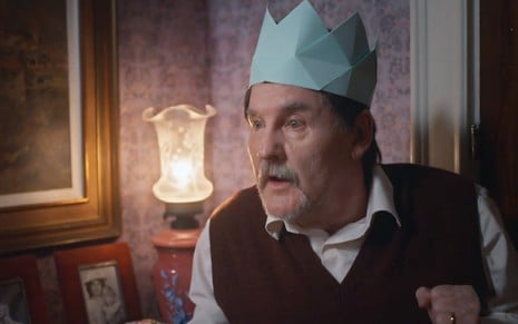 O ator Antonio Calloni como Matias com uma coroa feita de papel, em dobradura, em cena de Além da Ilusão