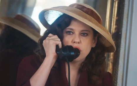 Bárbara Paz grava cena com expressão séria ao telefone, caracterizada como Úrsula da novela Além da Ilusão
