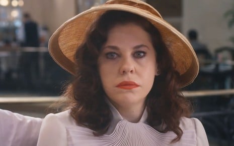 A atriz Bárbara Paz usa chapéu e um vestido claro caracterizada como Úrsula em cena de Além da Ilusão