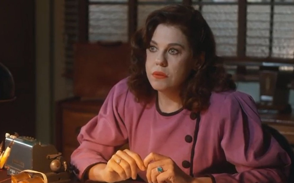 Úrsula (Bárbara Paz) está sentada em escritório e tem expressão de surpresa em cena de Além da Ilusão, novela das seis da Globo