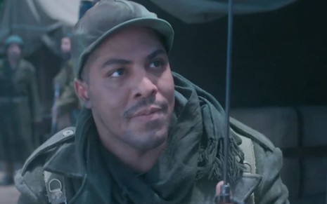 Matheus Dias, caracterizada como Bento, veste uniforme da Força Expedicionária Brasileira e dá um leve sorriso em cena de Além da Ilusão, novela das seis da Globo