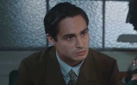 Joaquim (Danilo Mesquita) está sentado em seu escritório na tecelagem; ele aparenta estar irritado em cena de Além da Ilusão