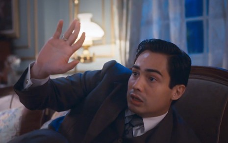O ator Danilo Mesquita, jogado em um sofá, faz o gesto de pare como Joaquim em cena de Além da Ilusão