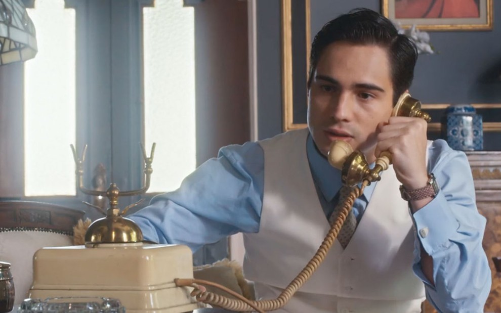 O ator Danilo Mesquita caracterizado como Joaquim fala ao telefone em cena de Além da Ilusão