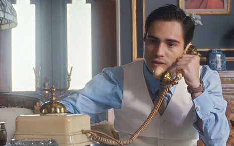 O ator Danilo Mesquita caracterizado como Joaquim fala ao telefone em cena de Além da Ilusão