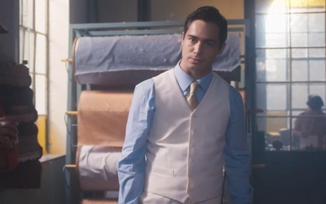 O ator Danilo Mesquita com expressão severa como o Joaquim no pátio de uma fábrica de tecidos em Além da Ilusão