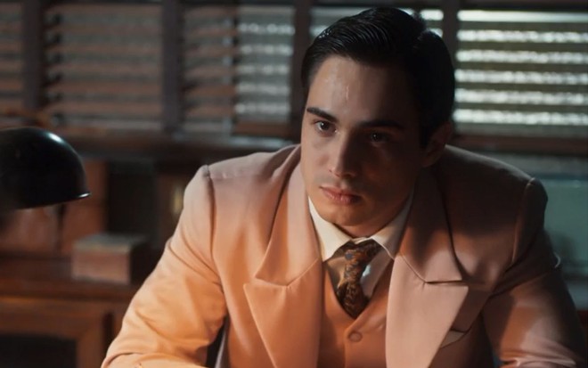 Joaquim (Danilo Mesquita) está sentado em escritório e tem expressão séria em cena de Além da Ilusão