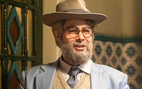 Rafael Vitti disfarçado de "velho barrigudo" em Além da Ilusão: ele usa peruca, sobrancelha e barba grisalha enquanto olha para a câmera