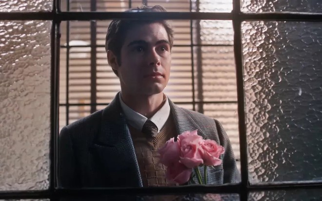 Rafael Vitti grava cena de Além da Ilusão usando terno e gravata e segurando flores em uma das mãos