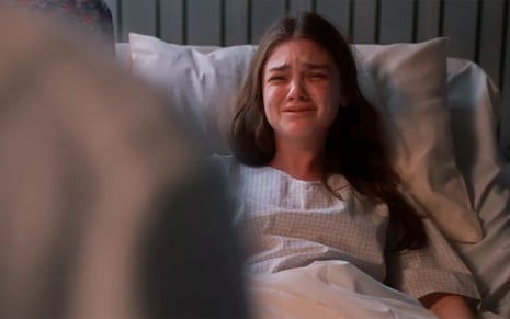 Debora Ozório tem os olhos cheios de lágrimas em cena de Além da Ilusão; a atriz está no leito de um hospital