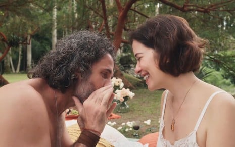 Eriberto Leão tem as duas mãos ao redor da boca; ele "conversa" com o coração de Paloma Duarte, a Heloísa, em cena de Além da Ilusão. A atriz sorri, encarando o colega.