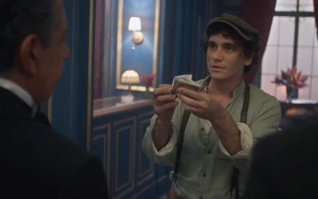 O ator Guilherme Prates, como Lorenzo, mostra um maço de cédulas de dinheiro em cena de Além da Ilusão