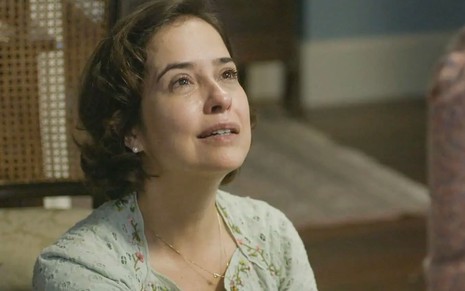 Paloma Duarte está agachada no chão; ela olha para cima, com os olhos cheios de lágrimas e a expressão perturbada, em cena de Além da Ilusão