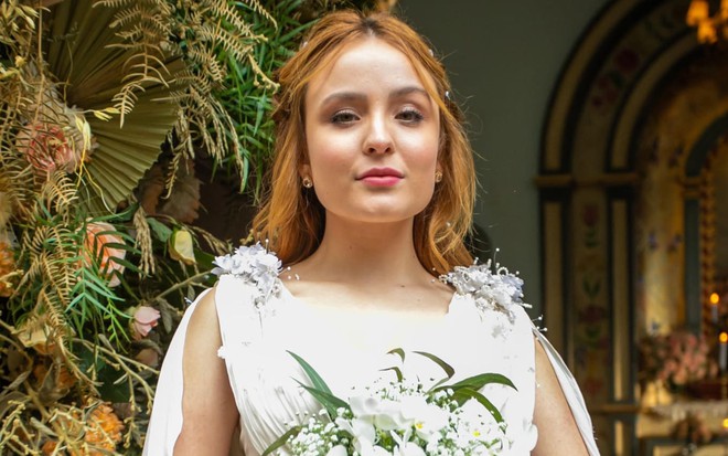 A atriz Larissa Manoela durante entrevista por chamada de vídeo; ela está sentada, olhando para a frente e conversando, com cara feliz