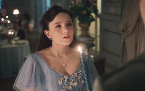 A atriz Larissa Manoela caracterizada como Elisa prestes a soprar uma vela azul, acesa, em cena de Além da Ilusão