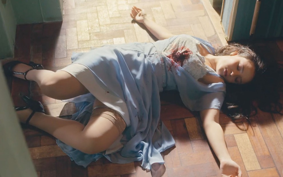 A atriz Larissa Manoela como Elisa, caída no chão, depois de levar um tiro no peito e com as roupas manchadas de sangue em cena de Além da Ilusão