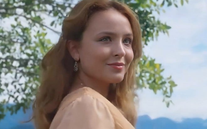 A atriz Larissa Manoela, ao ar livre, com uma árvore ao fundo, caracterizada como a Elisa em cena de Além da Ilusão