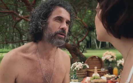 Eriberto Leão, caracterizado como Leônidas, está sem camisa; o ator, com cabelo e barba longos, encara Paloma Duarte --de costas para a câmera-- em cena de Além da Ilusão