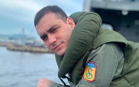 Guilherme Prates, caracterizado como Lorenzo, apoia-se na borda de um navio de guerra. Ele veste o uniforme da Força Expedicionária Brasileira em cena de Além da Ilusão