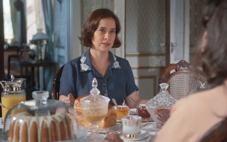 A atriz Paloma Duarte sentada à mesa de café da manhã como a Heloísa em cena de Além da Ilusão