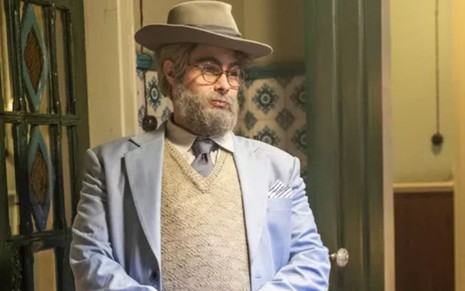 Davi (Rafael Vitti) está de chapéu, barba branca, óculos e enchimento na barriga em cena de Além da Ilusão
