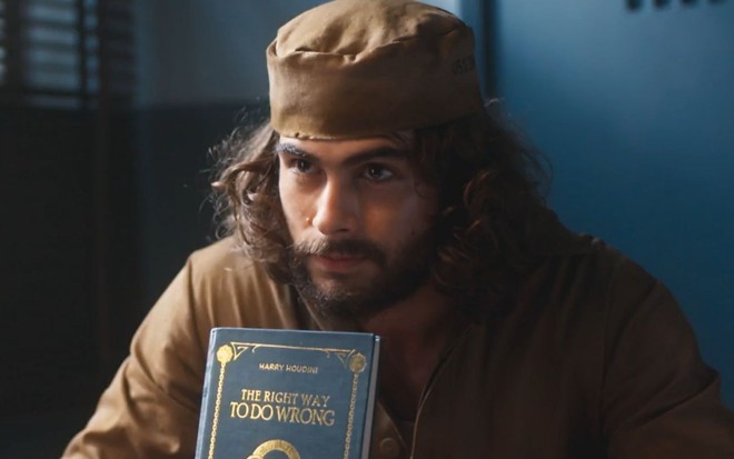 Rafael Vitti grava cena com expressão séria, segurando um livro, como Davi em Além da Ilusão