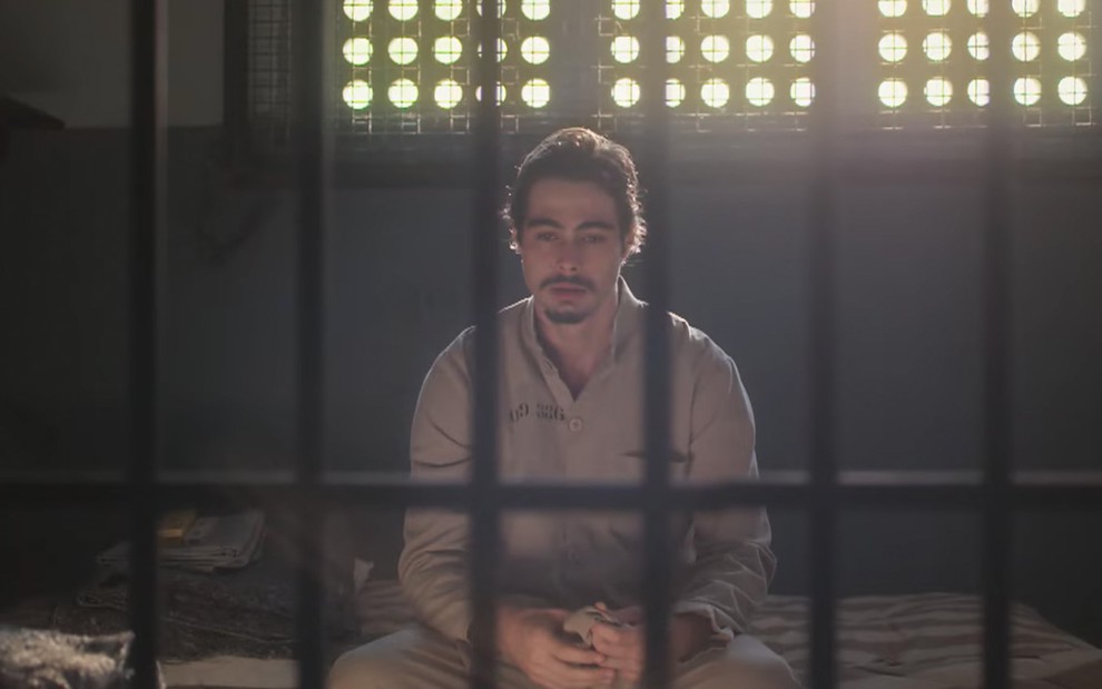 O ator Rafael Vitti como Davi com expressão triste e com roupas de presidiário em uma cela em Além da Ilusão