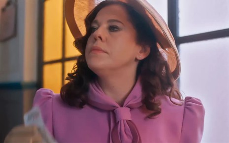 Bárbara Paz caracterizada como Úrsula em Além da Ilusão; atriz usa um sobretudo rosa e tem a expressão determinada em cena de Além da Ilusão
