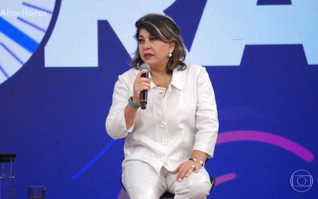 Com roupa branca, Roberta Miranda está sentada em um banquinho no palco do Altas Horas, da Globo