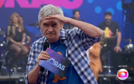 Serginho Groisman leva a mão à testa, como se fizesse força para enxergar, no Altas Horas ao vivo