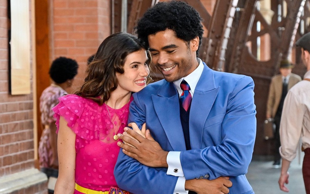 Com vestido pink, Camila Pitanga anda abraçada e sorrindo com Diogo Almeida em cena da novela Amor Perfeito