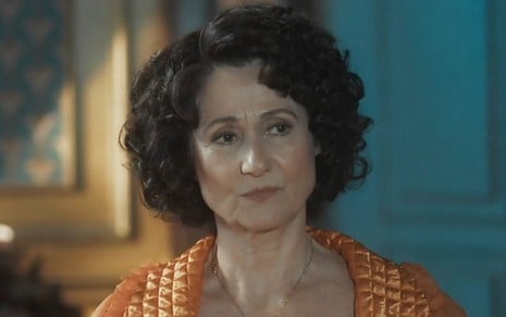 A atriz Zezé Polessa usa roupa laranja e exibe expressão de desgosto em cena da novela Amor Perfeito como Cândida