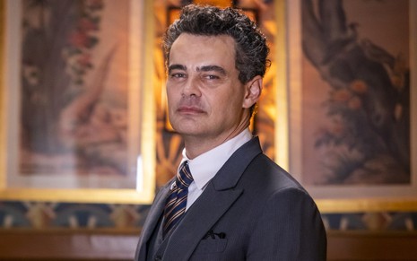 O ator Carmo Dalla Vecchia posa em cenário da novela Amor Perfeito usando terno e gravata caracterizado como Érico