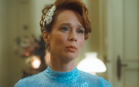 Mariana Ximenes caracterizada como Gilda; ela usa um vestido azul celeste e finge surpresa em cena de Amor Perfeito