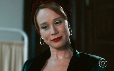 A atriz Mariana Ximenes está com cabelos preso, e usa batom vermelho e roupa escura em cena como Gilda em Amor Perfeito