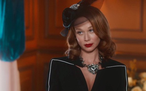 A atriz Mariana Ximenes usa vestido e chapéu pretos em cena da novela Amor Perfeito como Gilda
