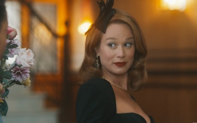 A atriz Mariana Ximenes com vestido preto, acessório de cabelo preto, com expressão de surpresa em cena de Amor Perfeito