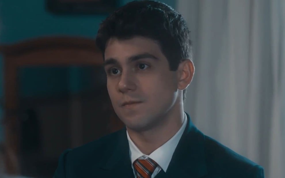 Daniel Rangel caracterizado como Júlio; ele usa um terno azulado e está sério em cena de Amor Perfeito