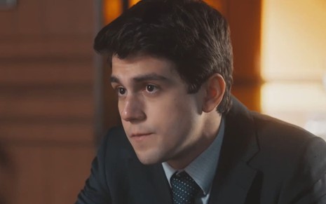 Daniel Rangel caracterizado como Júlio; ele usa um terno azulado e está sério em cena de Amor Perfeito