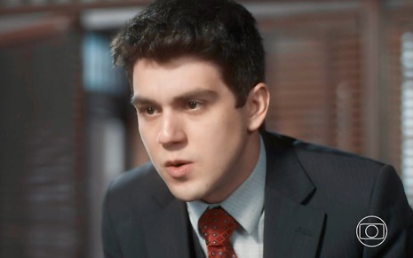 O ator Daniel Rangel está usando terno e gravata em cena da novela Amor Perfeito como Júlio