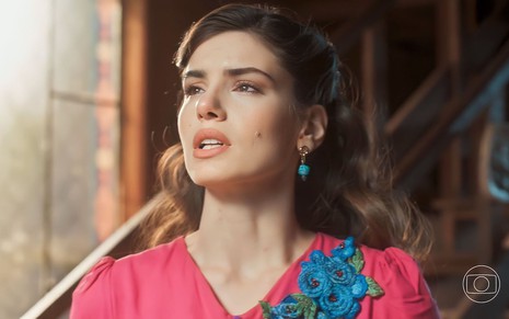 A atriz Camila Queiroz está com vestido pink, que tem detalhe azul no ombo, caracterizada como Marê em Amor Perfeito