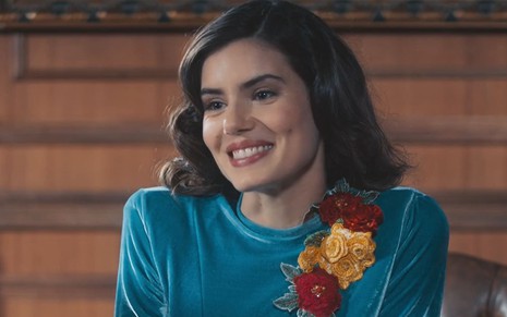 Camila Queiroz caracterizada como Marê; ela dá um sorriso apaixonado e usa um vestido azul em cena de Amor Perfeito