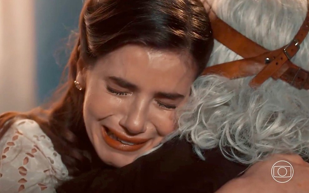 Camila Queiroz chora e tem os olhos fechados em cena de Amor Perfeito na qual abraça o ator Paulo Gorgulho
